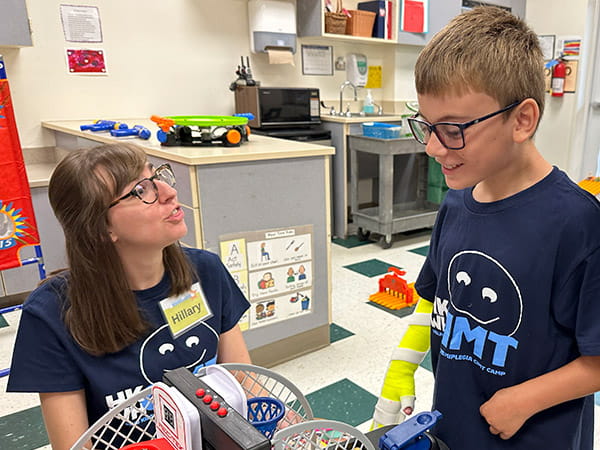 A Helping Kids with Hemiplegia therapist is playing a tabletop basketball game with a young camper.