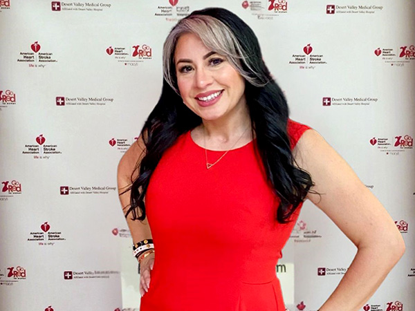 Brisa Alfaro is posing in a red dress in front of an American Heart Association Go Red For Women step and repeat backdrop.