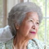 An older Chinese woman is looking out a window.