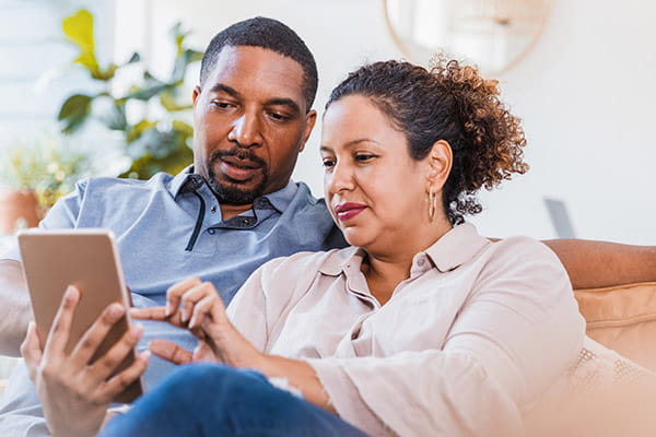 Un hombre y mujer adultos sentados en un sofá mirando juntos su tableta digital.