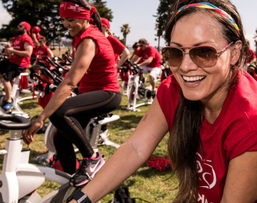 un grupo de personas con camisetas rojas en bicicletas estáticas en un parque
