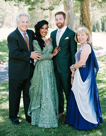 Steve, Dhivya, Danny and Deb are posing for a family wedding photo in an outdoor setting.