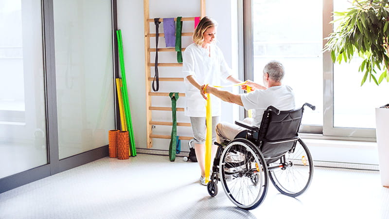 A young woman physiotherapist is working with an older man in a wheelchair.