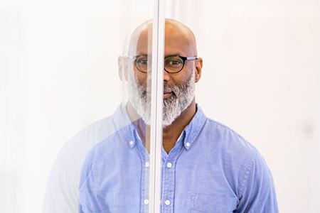 A bald middle-aged businessman and his mirror image on glass pane