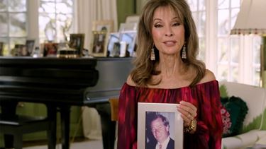 un fotograma de video de Susan Lucci en una sala con una foto enmarcada de su marido