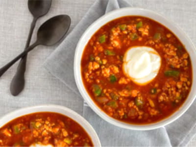 an aerial view of two bowls of chili with a dollop of yogurt and spoons arranged on grey table linens