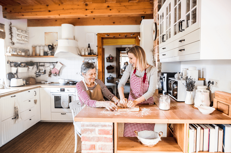 An older woman is kneading dough in a kitchen with family member. An older woman is kneading dough in a kitchen with family member.
